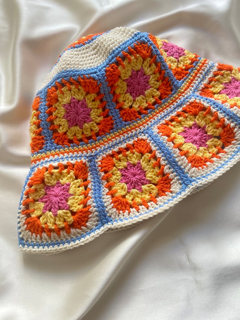 May include: A crocheted bucket hat with a colorful granny square pattern in shades of orange, yellow, pink, and blue.