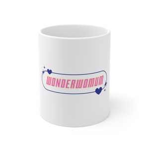 May include: White ceramic mug with a blue and yellow border around the text "WONDERWOMUM" in pink letters with two blue hearts and stars.