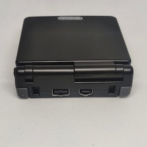 以下が含まれることがあります： ヒンジ付きの画面を持つ、黒いニンテンドーDS Lite携帯ゲーム機。コンソールは銀色のヒンジと、上部に銀色のニンテンドーロゴが付いています。