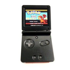 May include: A black Game Boy Advance SP handheld gaming console with a red accent on the bottom. The screen displays the Pokemon FireRed Version game title screen with a red dragon character.
