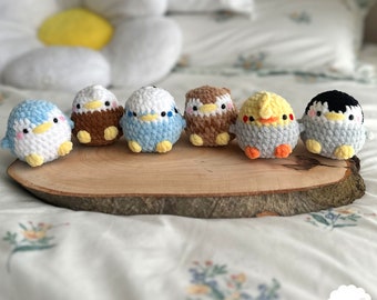 Può includere: Sette uccelli di peluche all'uncinetto in vari colori, tra cui bianco, marrone, blu, giallo e grigio, sono disposti su una fetta di legno. Gli uccelli sono tutti piccoli e hanno una forma rotonda. Gli uccelli sono tutti rivolti in avanti e hanno gli occhi aperti. Gli uccelli sono tutti seduti su una fetta di legno. La fetta di legno è su un copriletto bianco. Lo sfondo è un copriletto bianco con un motivo floreale.