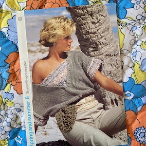 May include: A knitting pattern booklet featuring a photo of a woman wearing a grey knitted sweater with a trimmed V-neck. The cover text reads "Spring and Summer 8 Trimmed V-neck sweater".