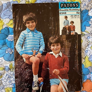 Könnte beinhalten: Ein Vintage-Strickmusterheft für Kinderpullover. Das Cover zeigt zwei Kinder in gestreiften und roten Pullovern mit dem Text "Patons Double Knitting 6348 8p 22-26 in. (56-66 cm)"
