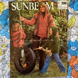 May include: A vintage knitting pattern for a hooded sweater, featuring a woman and two children wearing the sweater. The pattern is titled "Cherie" and is for a chest size of 66-97 cm.