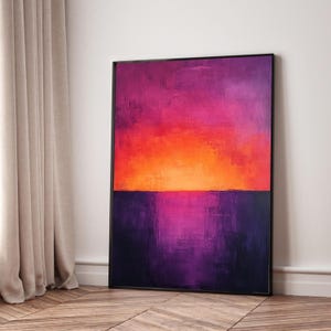 Puede incluir: Impresión artística abstracta que representa una escena de atardecer vibrante. La obra de arte muestra un degradado de colores, con un centro naranja y rojo intenso que transiciona a tonos púrpura y magenta profundos. La pieza enmarcada se apoya contra una pared blanca.