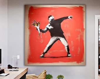 May include: A black and white stencil art print of a masked figure throwing a bouquet of flowers. The figure is silhouetted against a red background.