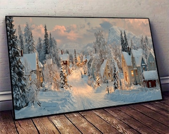 May include: A framed canvas print showing a snow-covered village scene. Houses with lit windows line a snow-covered road, surrounded by snow-laden trees and mountains. The sky displays soft pink and orange colours, possibly sunrise or sunset.