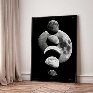 May include: Black framed art print featuring a grayscale depiction of the moon phases. The artwork showcases a series of moon images, with a large full moon in the background and smaller phases in the foreground. The print is displayed on a wooden floor.
