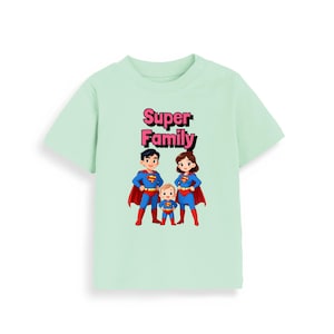 May include: A pale green baby t-shirt with the text "Super Family" in pink and black. The shirt displays a cartoon illustration of a family in superhero costumes, complete with red capes and blue suits.