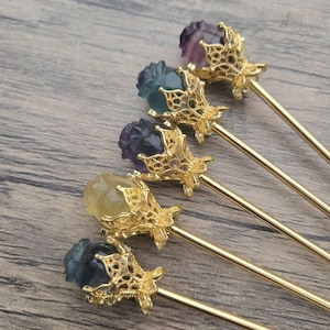 May include: Set of six gold-tone hair sticks with a decorative filigree design. Each stick features a carved gemstone rose in a variety of colors, including purple, green, and yellow.
