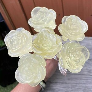 May include: A bouquet of six translucent, pale yellow, resin rose flower sculptures. The roses are arranged in a cluster and have a glossy finish.