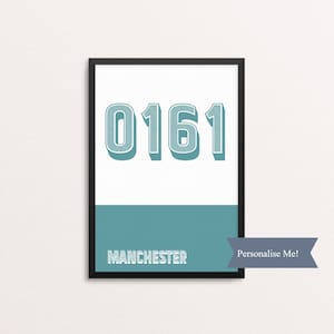 May include: A framed print with a black frame and a white background. The print features the number 0161 in large, teal blue font with a white outline. The word "MANCHESTER" is printed in white below the number. The text "Personalise Me!" is printed in white on a teal blue ribbon.