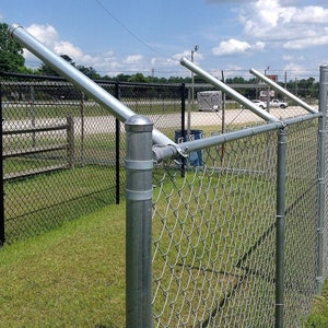 May include: A silver chain link fence with two metal poles and a horizontal metal bar. The fence is attached to the poles with metal brackets. The fence is in front of a grassy area.