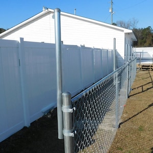 May include: A white vinyl fence with a chain link fence attached to it. The fence is in front of a white building with a wooden deck.