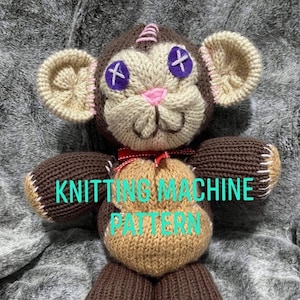 May include: Knitting machine pattern for a brown and beige monkey toy with pink ears, a red bow, and purple eyes with an X on each. The text "KNITTING MACHINE PATTERN" is visible on the toy.