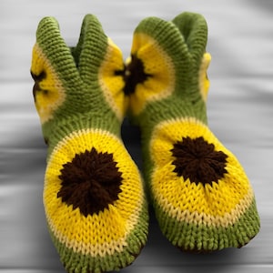 May include: A pair of green, yellow, and brown knitted slippers with a sunflower design.