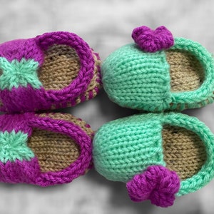 May include: A pair of knitted baby booties in pink and green with a brown sole. One pair has a flower on the top.