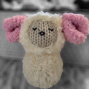 May include: A white and pink knitted plush toy shaped like a sheep with closed eyes and a black nose.