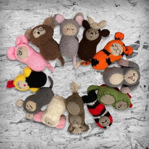 May include: Twelve knitted animal plushies in various colors and designs, including a pig, a rooster, a monkey, a tiger, a rabbit, a snake, a horse, a goat, a dog, a cat, a mouse, and an ox. The plushies are arranged in a circle on a white background.