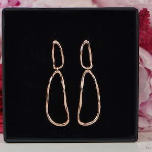May include: Rose gold double hoop earrings with a twisted design. The earrings are displayed in a black box.