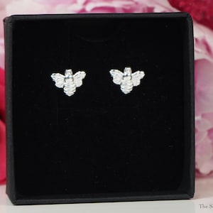 Peut inclure: Une paire de boucles d'oreilles en argent en forme d'abeille dans un écrin à bijoux en velours noir. Les boucles d'oreilles sont petites et délicates, avec un motif d'abeille détaillé.