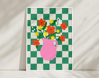 May include: A framed art print featuring a pink pitcher filled with red, yellow, and white flowers. The background is a green and cream checkerboard pattern. The artwork is displayed against a neutral wall with shadows.