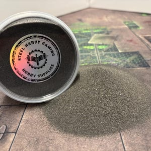 Può includere: Un contenitore di sabbia grigio scuro per modellismo ferroviario o altri progetti di hobby. Il contenitore ha un'etichetta che recita "Steel Harpy Gaming Hobby Supplies".