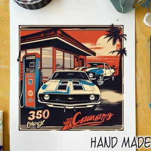 May include: A vintage-style illustration of two white and blue Chevrolet Camaros parked in front of a gas station. The illustration has a sunset background with palm trees and the text "350 Chevy" and "Camaro".