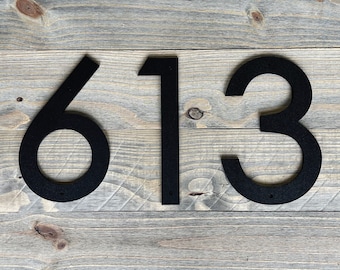 May include: Black metal house numbers 613 on a wood background.