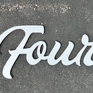 May include: A brushed silver metal sign displaying the word "Four" in a cursive font. The sign is cut from a single piece of metal and is set against a dark gray textured background.