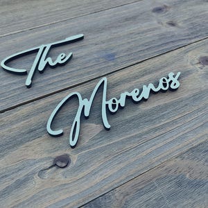 May include: The words "The Morenos" are written in white cursive on a wooden surface.