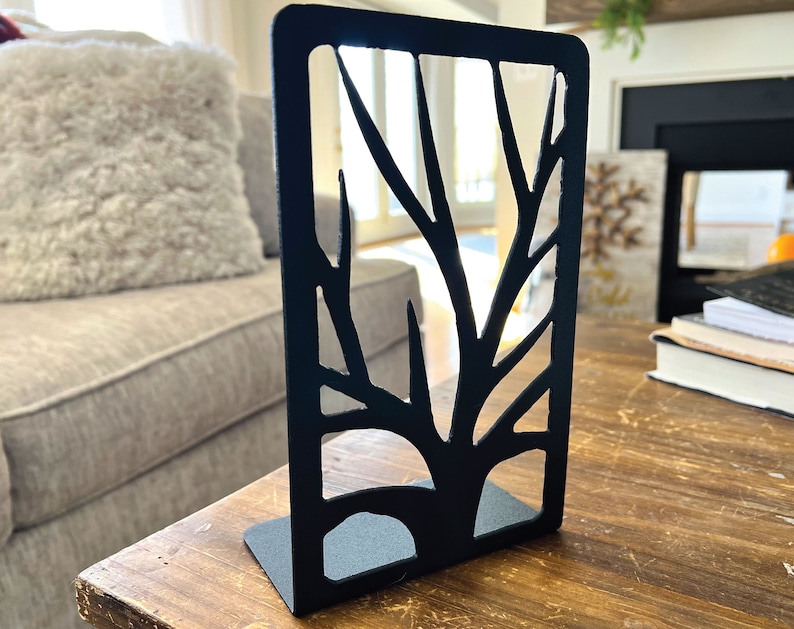 May include: Black metal bookends shaped like a tree with a cutout design. The bookends are on a wooden table.
