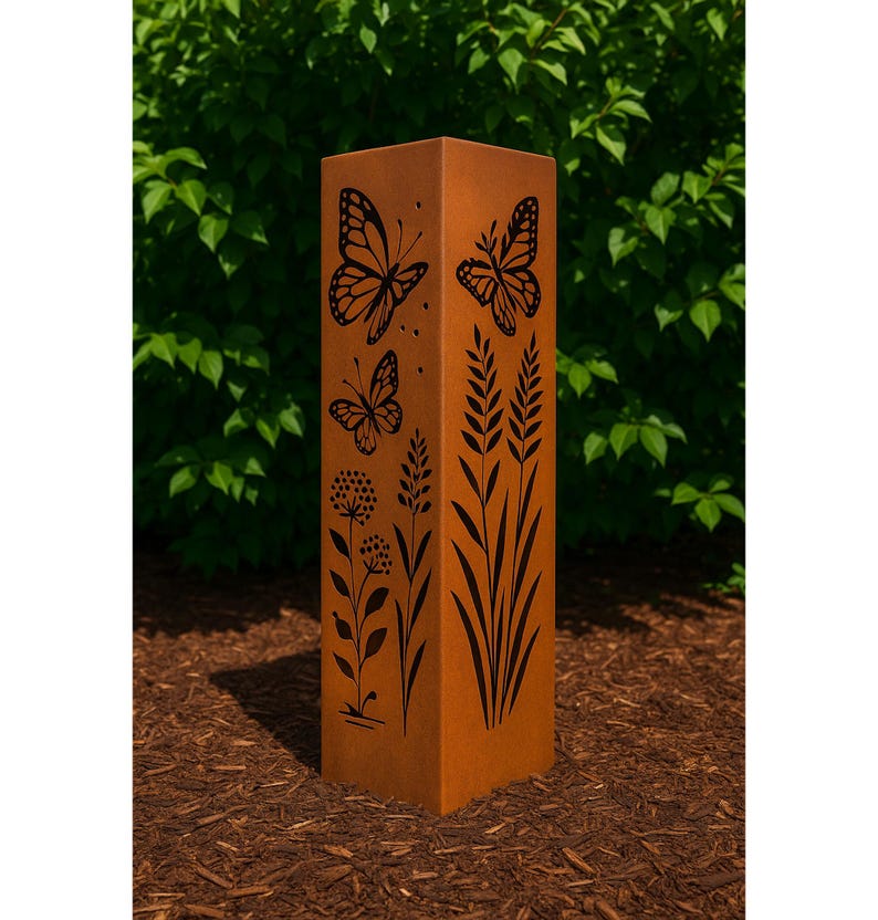 K&ouml;nnte beinhalten: Ein hoher, rechteckiger Gartenpfeiler aus rostorangefarbenem Metall. Der Pfeiler weist schwarze Ausschnitte von Schmetterlingen, Blumen und hohem Gras auf. Der Pfeiler steht auf einem Bett aus braunem Mulch, mit gr&uuml;nem Laub im Hintergrund.