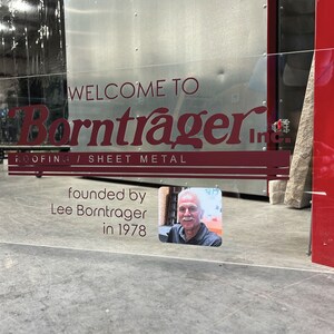 Pu&ograve; includere: Segno in acrilico trasparente con testo bordeaux: "WELCOME TO Borntrager Inc. ROOFING / SHEET METAL". Include una foto di Lee Borntrager e il testo "fondata da Lee Borntrager nel 1978".