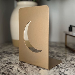 May include: Gold metal bookends with a crescent moon cut-out design.