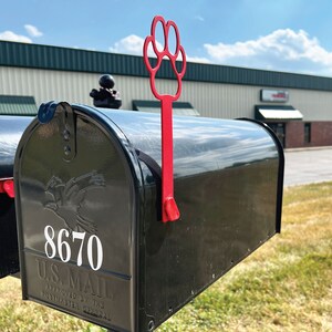 Może przedstawiać: Czarna skrzynka pocztowa z czerwoną flagą w kształcie łapy. Skrzynka pocztowa ma numer 8670 i tekst "U.S. MAIL APPROVED BY THE POSTMASTER GENERAL".