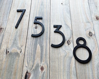 May include: Black metal house numbers 7538 on a wood background.