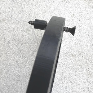 May include: A close-up of a black metal ring with two screws. The ring is attached to a wall or other surface.