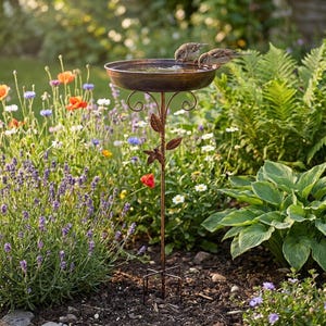 Peut inclure: Un bain d'oiseaux en métal de couleur bronze doté d'un bassin circulaire peu profond soutenu par un pied fin orné de feuilles décoratives et de volutes. Deux petits oiseaux bruns sont posés sur le bord du bassin et boivent de l'eau.