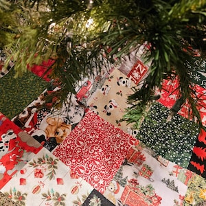 May include: A patchwork Christmas tree skirt with a variety of holiday-themed fabrics, including dogs, stars, and snowflakes. The skirt is made of red, green, white, and black fabrics.