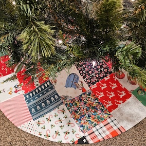 May include: A patchwork Christmas tree skirt with a variety of holiday-themed fabrics, including candy canes, reindeer, and a blue house. The skirt is made of a variety of fabrics, including cotton and flannel.