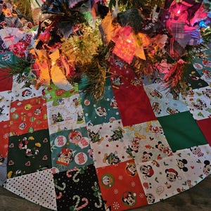 May include: A patchwork Christmas tree skirt with a red, green, and white color scheme. The skirt is decorated with a variety of Disney characters, including Mickey Mouse and Minnie Mouse.