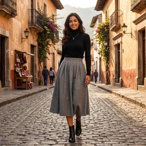 May include: A black long-sleeved turtleneck jumper paired with a grey pleated midi skirt made of a textured fabric. The outfit is completed with black ankle boots. The skirt features a high waist and a flared silhouette that falls below the knee.
