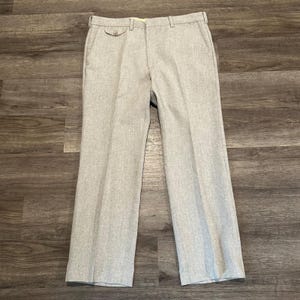 May include: Light gray dress pants with a straight leg. The pants have a button closure and pockets. The fabric has a subtle texture. The pants are laid flat on a wooden surface.