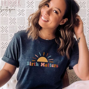 May include: A heather navy blue t-shirt with a colorful sunrise graphic and the text "Birth Matters".