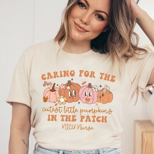 May include: A beige t-shirt with a graphic of pumpkins and the text "Caring for the cutest little pumpkins in the patch NICU Nurse".