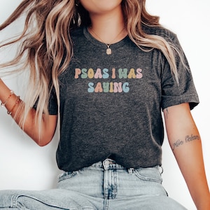 May include: A dark grey t-shirt with the text "PSOAS I WAS SAYING" in colourful, rounded letters.
