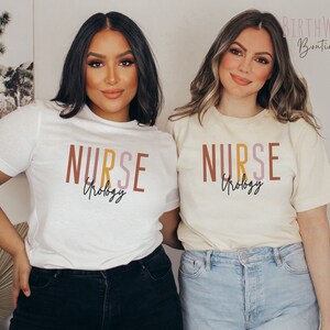 May include: Two people wearing white and cream short-sleeved t-shirts with the text "NURSE Urology" in colorful letters. The text is in a layered, stacked font style.