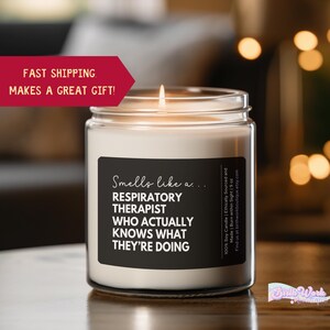 May include: A lit white soy candle in a glass jar. The black label reads "Smells like a... RESPIRATORY THERAPIST WHO ACTUALLY KNOWS WHAT THEY'RE DOING." The candle is 19 oz. and is ethically sourced.