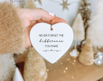 May include: White ceramic heart ornament with the text "Never forget the difference you make" in black script. The ornament is hanging from a gold string.